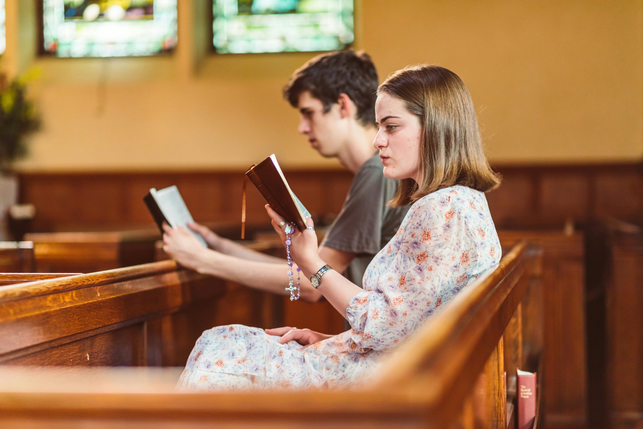 Two young adults seated in a church pew, deeply engaged in prayer and reading.